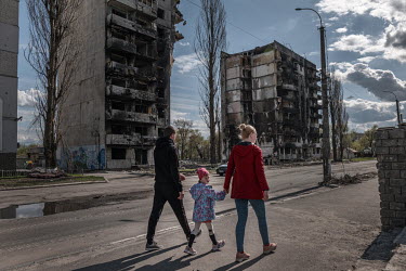 A couple and a child walk past destroyed apartment buildings.