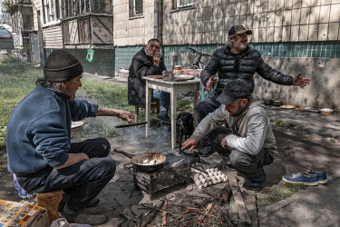 A group of friends cook a meal on an open fire outside their flats. The other side of the building was completely destroyed. One of them says: "We are survivors. Five of us stayed here during everythi...