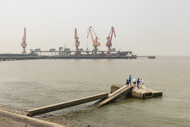 People fishing in the Yangtze River near the Port of Nantong where grain is being unloaded from a bulk transporter and loaded onto smaller river barges at the Nantong Cereals & Oils Transfer Co. facil...