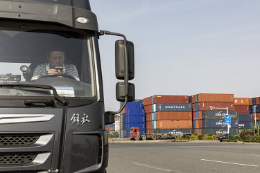 A truck driver looks at his phone while sitting in his cab at the Qingdao Qianwan Container Terminal.