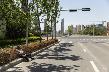 A man falls asleep while resting by a road in a new residential development zone.