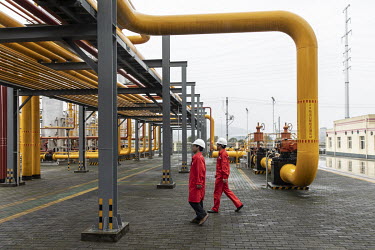 Workers walk amongst pipework and storage tanks stand at a shale gas collection and transfer facility at the Fuling shale gas project site, operated by Sinopec Chongqing Fuling Shale Gas Exploration a...