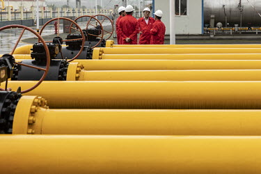 Workers talking amongst pipework and storage tanks stand at a shale gas collection and transfer facility at the Fuling shale gas project site, operated by Sinopec Chongqing Fuling Shale Gas Exploratio...