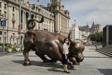 A woman poses for pictures while standing next to the Bund Bull statue.