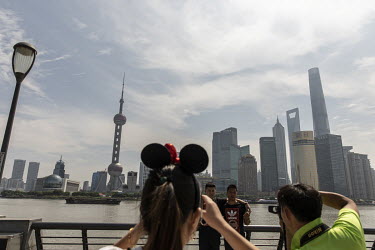 Tourists take pictures along the Bund with the Pudong District behind them.