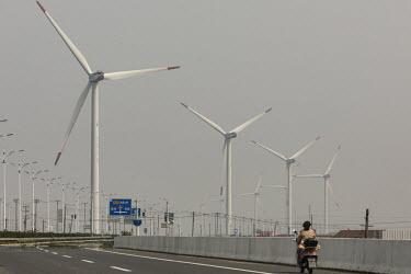 A rider on a scooter passes a wind farm operated by China Huaneng Group.
