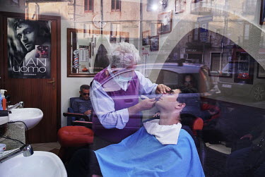 A barber shaving a customer in the town centre.