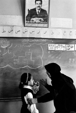 A teacher and a pupil stand beneath a portrait of Saddam Hussein at a school for deaf children.