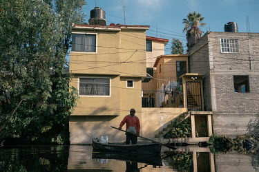 A farmer stands in his boat on a canal in an urbanised area of Xochimilco.