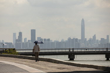 A man walks along the Shenzhen Bay promenade with a view of the city beyond.