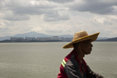 A man rides a bicycle along the Shenzhen Bay promenade with a view of Hong Kong across the water.
