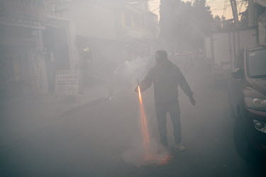 A man lights up a firework while the street fills up with smoke during a festivities in the San Diego neighbourhood.