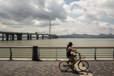 A woman rides a bicycle along the promenade near the Shenzhen Bay Bridge.