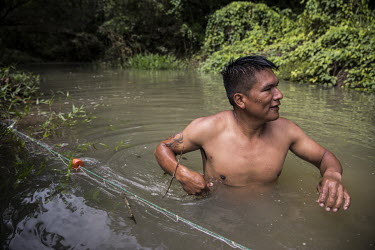 A man wades chest deep into the Rio Bobonaza in order to check fishing nets laid earlier.