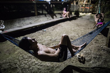 A man sleeping in a hammock. Typically, the living area is outside, around the hammocks. After a day of working in the humid heat people will rest and socialise for a few minutes before going to sleep...