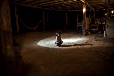 A boy squats inside a building lit by candles and torchlight.