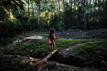 A girl crosses a gully using a length of wood.