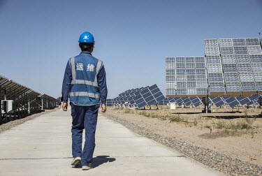 An employee walks past photovoltaic panels at the Golmud Solar Park on the outskirts of the city. China leads the world in solar energy production with most its solar power generated in its western pr...