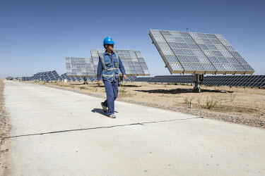 An employee walks past photovoltaic panels at the Golmud Solar Park on the outskirts of the city. China leads the world in solar energy production with most its solar power generated in its western pr...