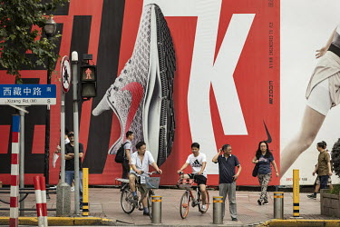 People wait to cross a street in front of a Nike training shoe advert.