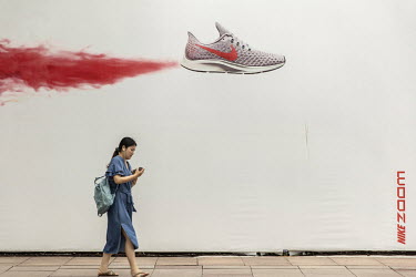 A pedestrian walks past a Nike training shoe advert.