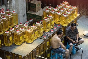 Shop owners sit in front of containers of cooking oil at a food market.