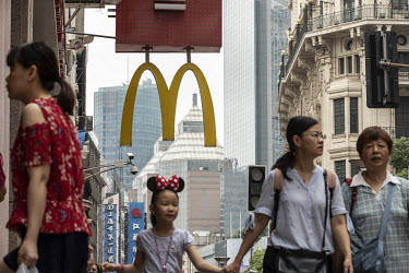 Pedestrians walk past the golden arches hanging in front of a McDonald's restaurant.