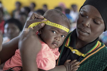 A child, being held by its mother, is weighed and measured at a health centre where their growth and development is monitored.
