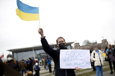A Ukrainian activist in front of the Chancellor's office waves a Ukrainian flag while holding a placard that reads: '5000 helmets That's not enough', decrying Germany's military assistance following t...