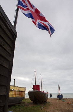 A Union Jack flag flies above the fishing boats (trawlers) moored on the shingle beach at Hastings.