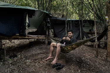 Soe Myint Moe, a People's Defence Force (PDF) soldier, sits in his hammock outside his shelter on a PDF base in an undisclosed location in Karen State.