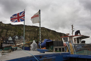 A Union Jack flag and a cross of St George flag flying above the fishing boats (trawlers) moored on the shingle beach at Hastings.