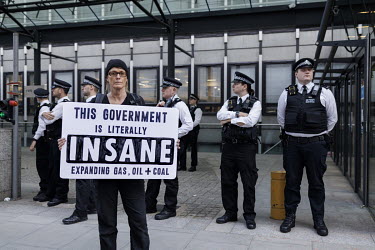 A woman stands infront of a line of police officers holding a placard that reads: 'This Government is literally INSANE', during a protest in Westminster outside the Department for Business, Energy and...