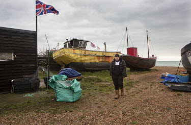 Alfie White, a young fisherman, walking past fishing boats (trawlers) moored on the shingle beach at Hastings.