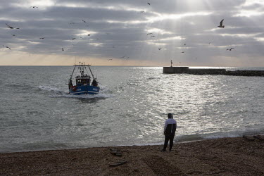 Alfie White waits on the shingle beach as his father returns in his trawler from an all night fishing trip.