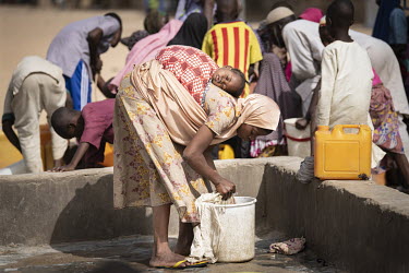 A woman washing clothes, with a sleeping child strapped to her back, in Teacher's Village IDP camp, home to 20,000 civilians who fled the conflict with Boko Haram in Borno State.