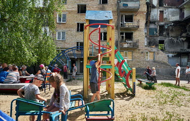 Children playing outside a bomb damaged apartment building. Behind them a group of adult residents are having a meeting where they wrote a joint letter to their politicians asking that their electrici...