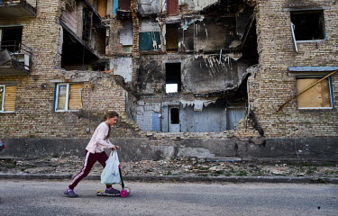 The girl rides a kick scooter past a destroyed apartment block as life slowly returns to the village of Horenka.