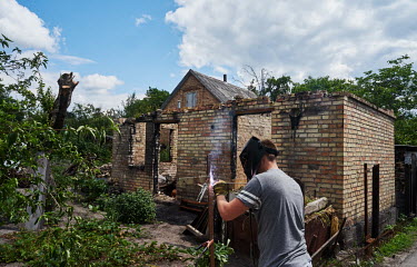 A man welding an fence post beside a house destroyed by Russian bombing as life slowly returns to the village of Horenka.