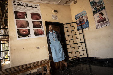 Kasika Mkwakti, nurse and midwife at the Maramba Clinic, standing beside a Female Genital Schistosomiasis (FGS) health education poster.Female Genital Schistosomiasis (FGS) is a waterborne parasitic d...