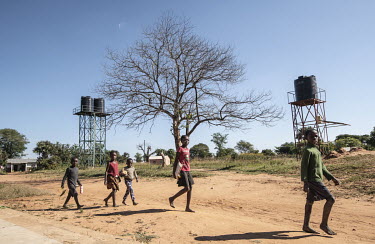 School children walk past storage tanks of fresh drinking water from wells provided by WaterAid.  Female Genital Schistosomiasis (FGS) is a waterborne parasitic disease affecting women. Symptoms inclu...