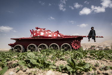 A farmer sits on a destroyed Russian tank, that has been repainted in red, in his potato field.