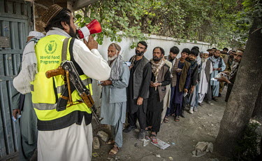 A security guard makes an announcement to people queuing at a World Food Programme (WFP) distribution centre near Madina Bazaar in central Kabul.
