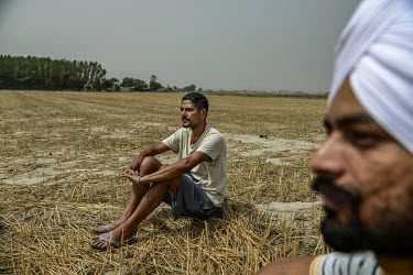 Ranjit Singh sits with his nephew in a harvested field on his farm.