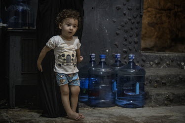 Fouad Ibrahim (13 months) stands near containers of drinking water that his family have delivered to the damp cellar where they live in Saida. Inflation surpassed 137 percent in August 2021 which make...