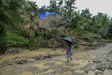 A resident, holding an umbrella, as she walks past houses destroyed by a landslide in Gilgal village near Moulhoi.