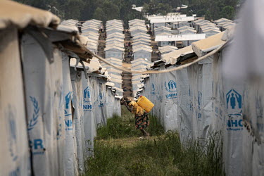 A woman carriews a large container of water past the UNHCR tents at the Kigonze IDP Camp.  There are at least 5.5 million internally displaced people (IDPs) in the DRC, mostly in the eastern provinces...
