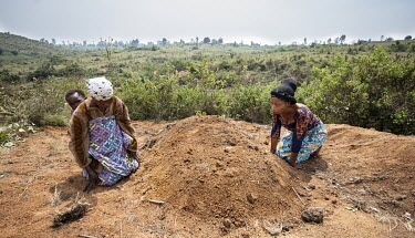 Dosabi Umani (38, L) with her baby Hepe (1) and Chantal Safari (39), the two wives of Jonathan Mandevu, kneel at his graveside at Tsere IDP camp. Jonathan was hacked to death by an ethnic militia when...