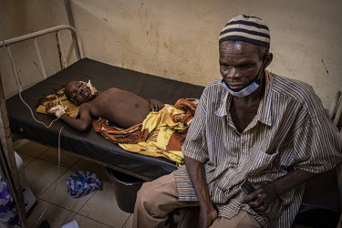 A man sits beside a child being treated at the Kaya Regional Hospital. The hospital is operating at over 100% capacity, often with three patients per bed.  Once considered 'safe', Burkina Faso (meanin...