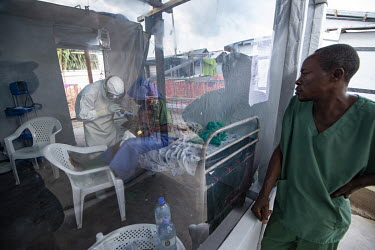 A colleague looks through the a barrier window as a medical worker tries to insert a cannula into a child who is held by an ebola survivor, who has a level of immunity, in an isolation cube at the Ben...